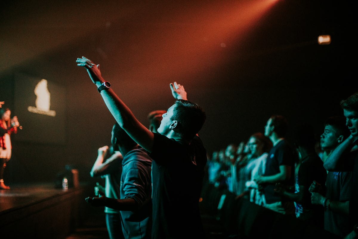 Worshippers with hands raised under warm, low stage lighting at a prayer gathering